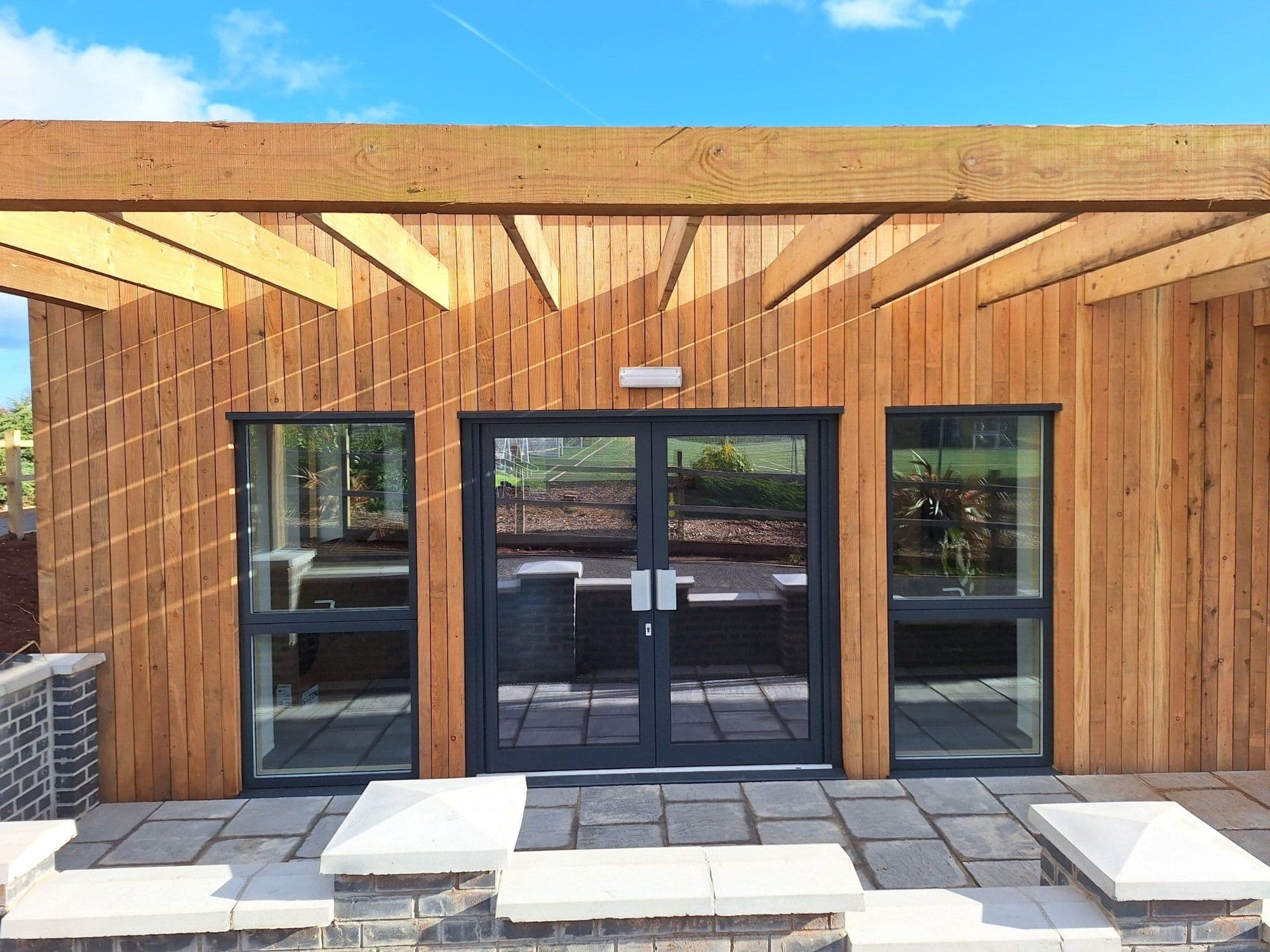 Timber-clad off-site school building with glazed double doors under a timber canopy