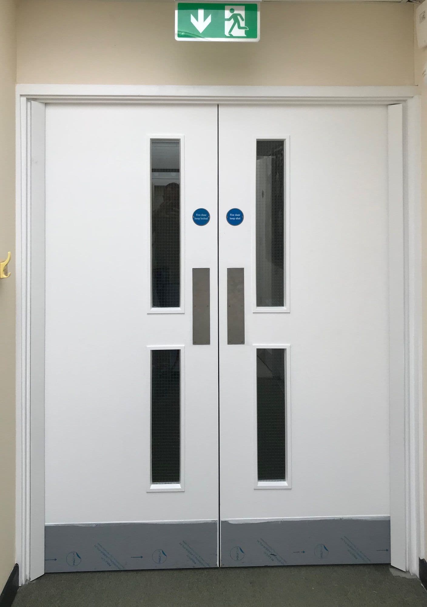 New white double fire doors with vision panels below an emergency exit sign